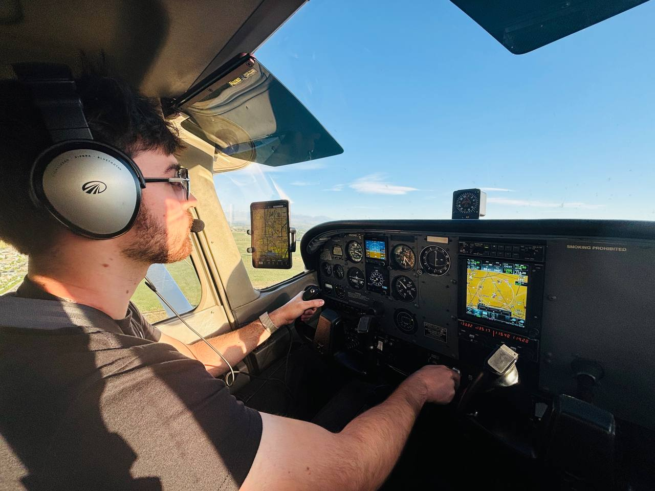 The author flying a small single-engine aircraft, wearing a headset with one hand on the yoke and the avionics panel lit ahead